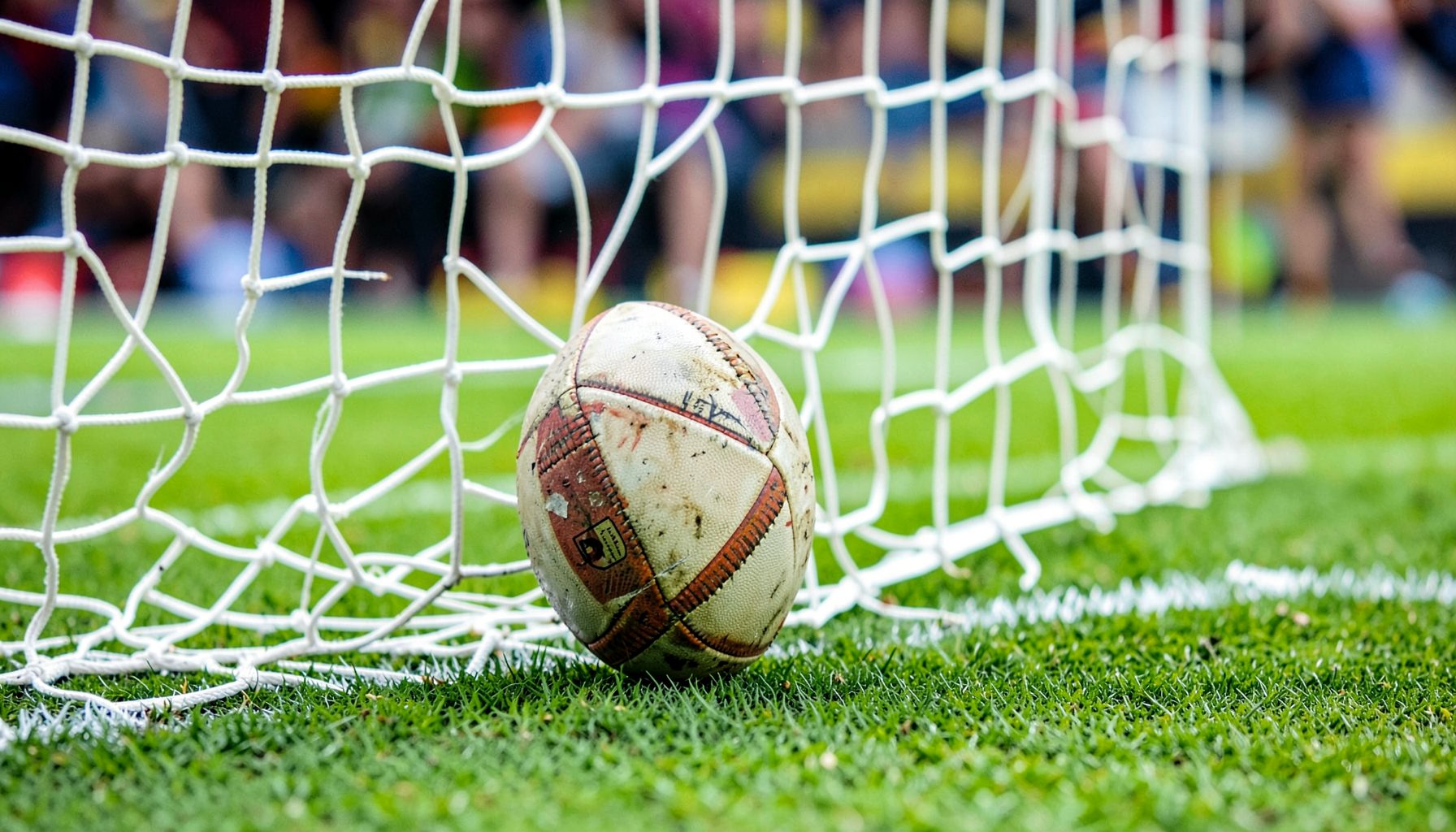 Close-up of a football striking the back of the net, vivid green pitch, celebratory mood